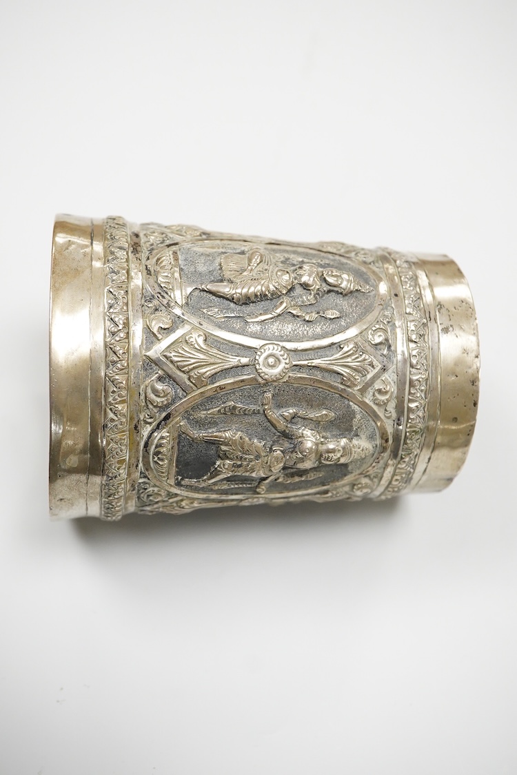A 19th Century Indian white metal mug, embossed with deities, 11.1cm.